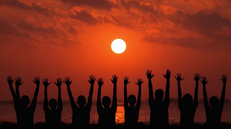 Silhouetted Figures Celebrating at Sunset with Outstretched Hands Against a Vibrant Orange and Red Sky Reflecting on Water