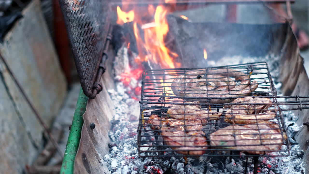 Smoke rise from hot coals as fat drips from lamb chops and traditional sausage