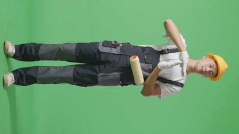 full body of asian man painter wearing safety helmet looking at camera and showing time out hands gesture while standing in the green screen background studio