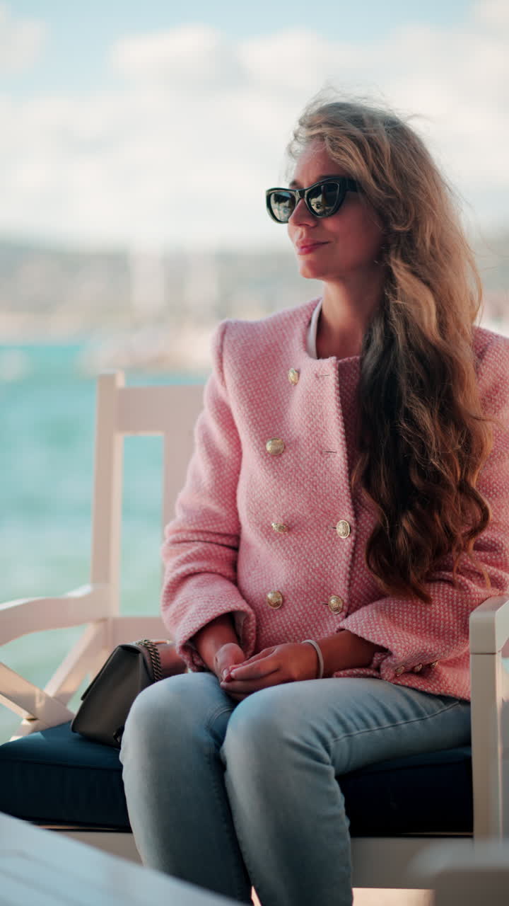 Kvinde i en pink blazer, der sidder på en stol på stranden i Antibes, Frankrig. Lodret