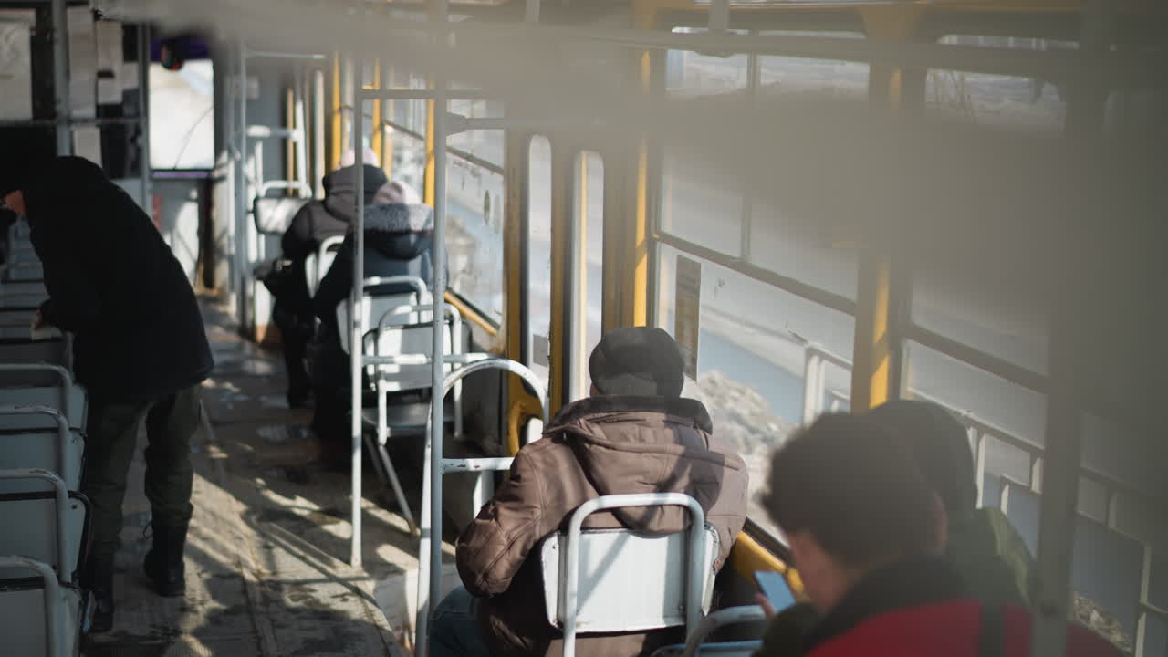 high angle interior on moving bus during winter commute, passengers seated, vehicle pauses at stop then rolls forward as entrant boards, cold sunlight through yellow windows