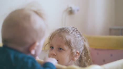 little-brother-looks-at-sister-hiding-in-playpen-at-home