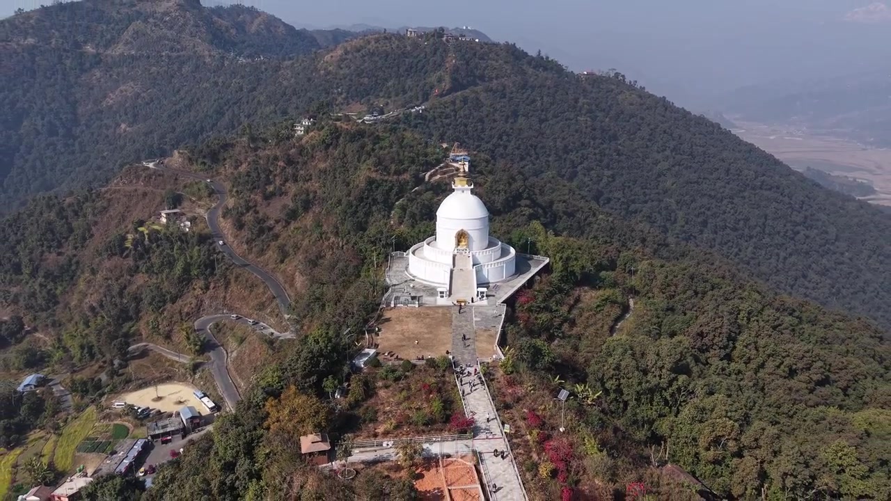 Prospettiva drone che cattura la cupola bianca e le scale della Shanti Stupa con una strada tortuosa a lato.
