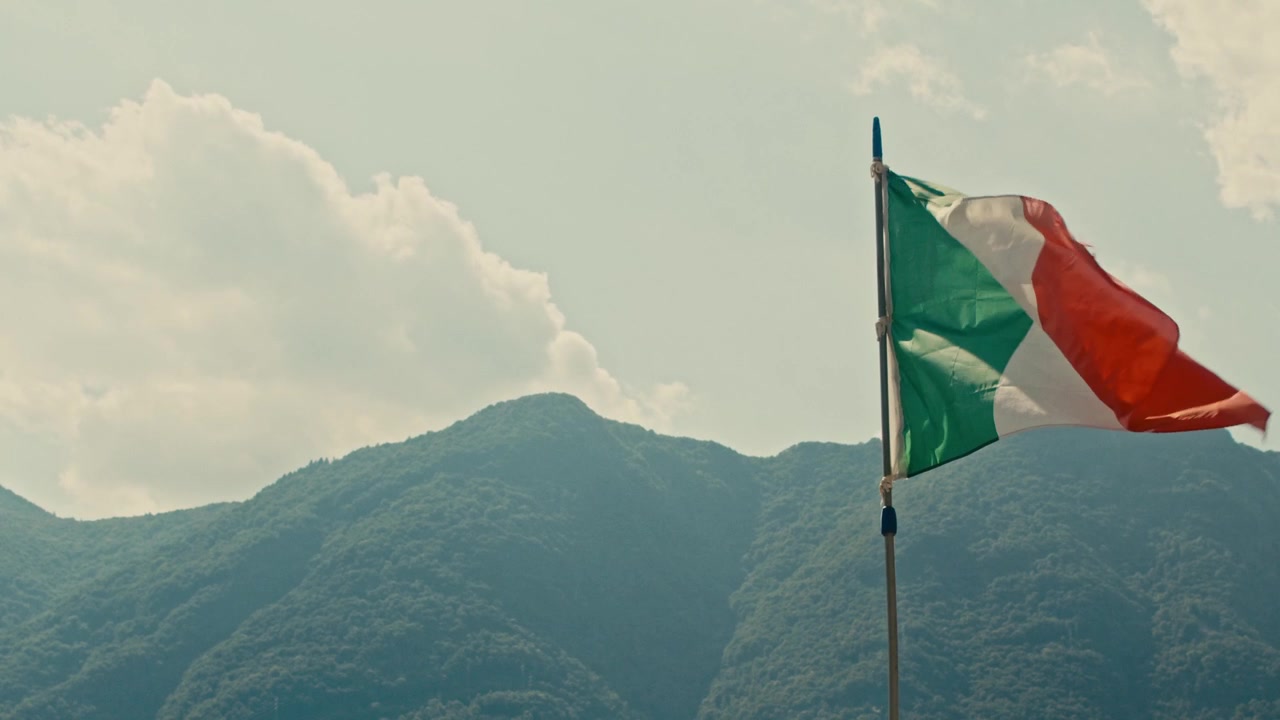 Bandiera tricolore italiana che sventola davanti alle montagne boscose del Lago di Como.