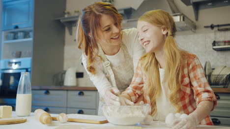 happy cheerful mother with her cute schoolgirl daughter talking and laughing while making a daugh for cookies and muffins in the cozy modern kitchen. indoors