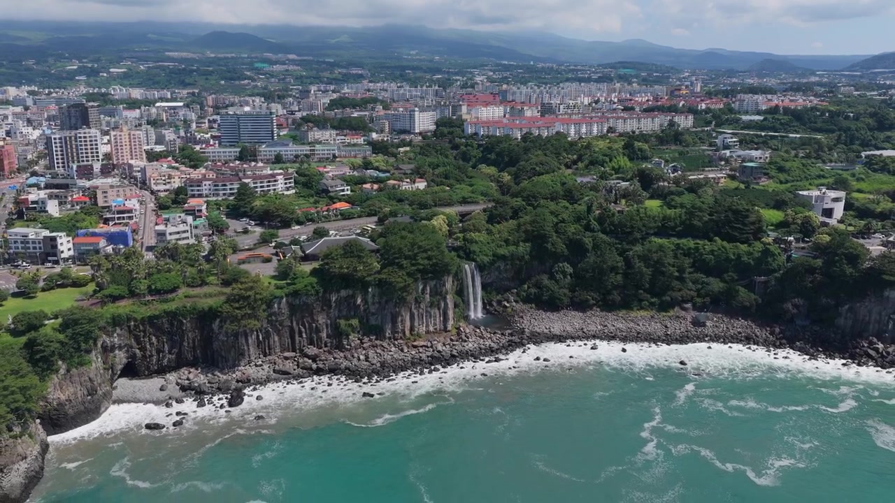 Cascata di Jeongbang e la città turistica di Seogwipo sull'isola di Jeju, Corea del Sud. Ripresa aerea con allontanamento.
