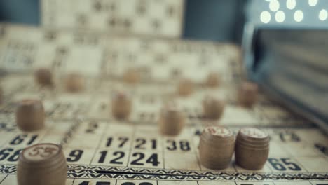 macro video of a bingo board, studio lights, 120 fps, slow motion, wooden chip digits, raw footage, vintage lottery desk game, card numbers, crane pull back smooth movement