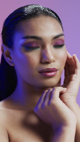 vertical video of biracial woman with black hair and make up touching face, copy space, slow motion