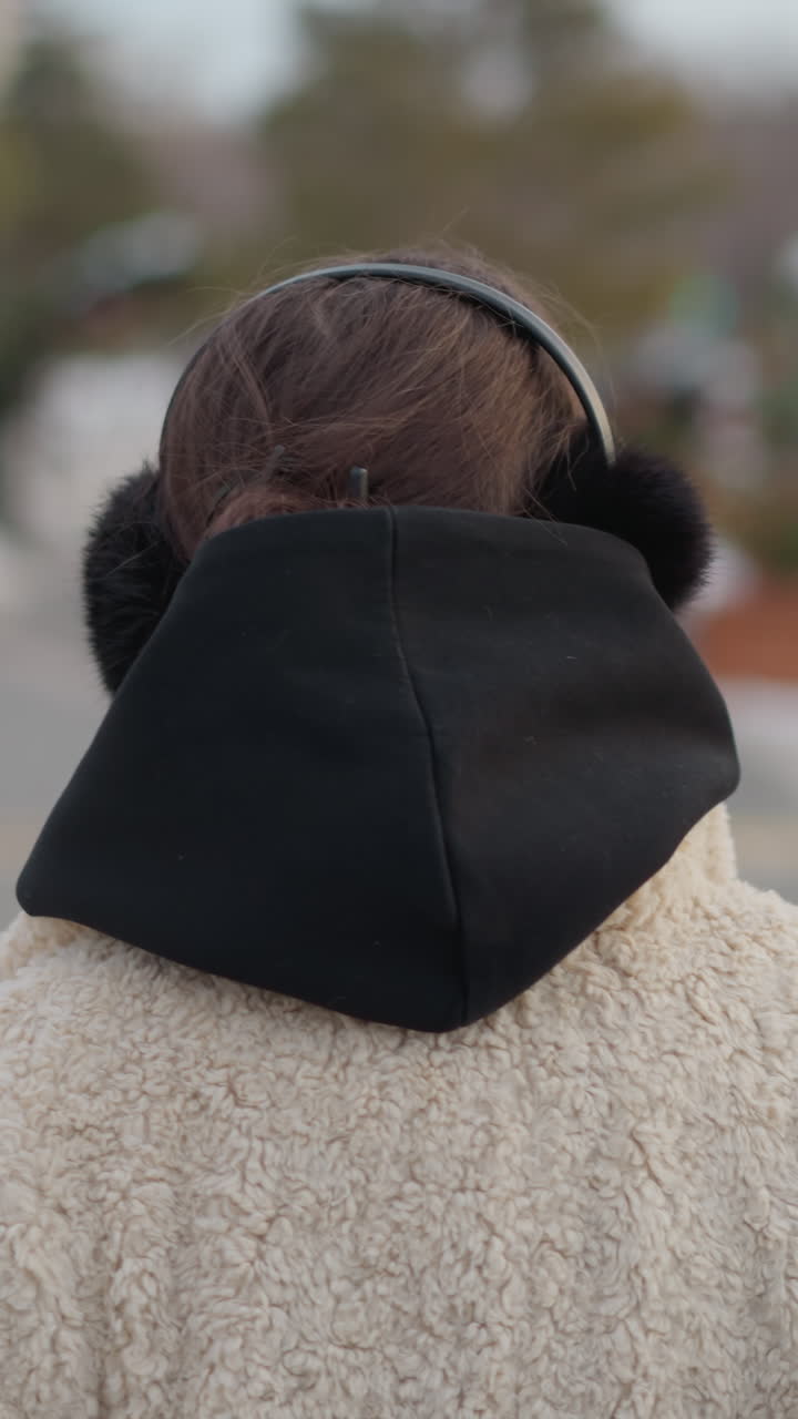 Youthful winter moment, Girl enjoys chilly city walk, Young woman in cozy coat amidst winter city scene, Teenage girl with fluffy jacket and earmuffs strolling through snowy urban environment