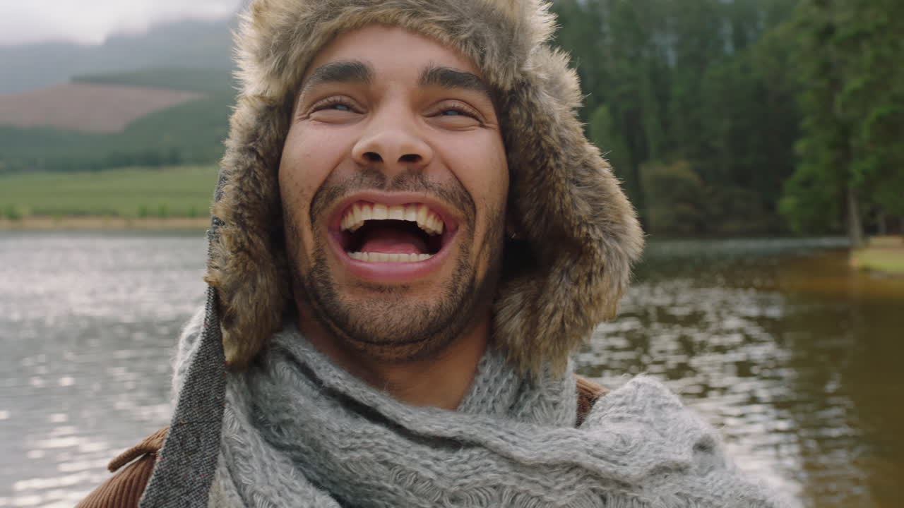retrato joven riendo sintiéndose feliz usando sombrero de piel al aire libre en la naturaleza junto al lago