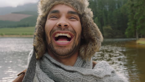 portrait young man laughing feeling happy wearing fur hat outdoors in nature by lake