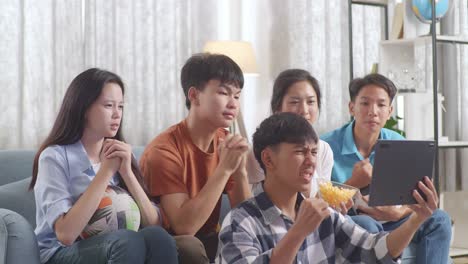 asian teenagers cheering and watching football game on tablet at home