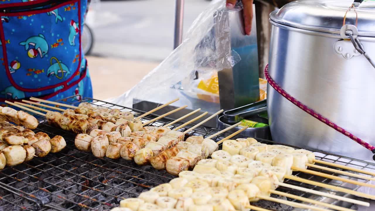 A street vendor grills bananas on skewers at a bustling market in Phuket, showcasing vibrant colors and lively atmosphere