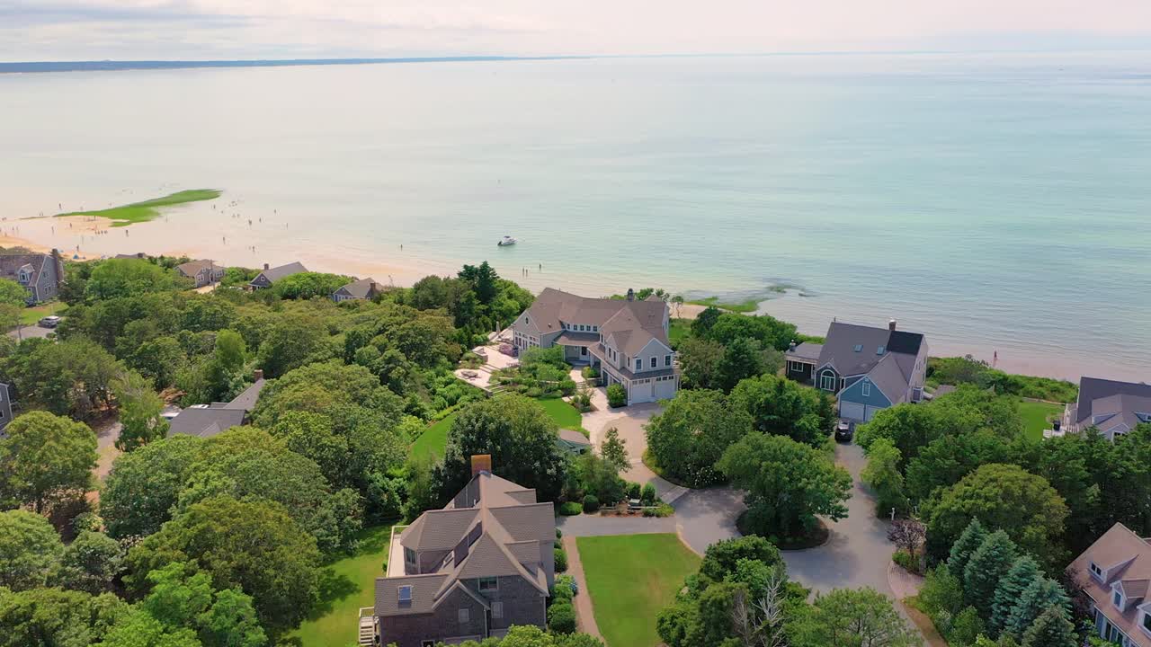 Aerial view reveals a spacious home with manicured grounds set beside the ocean, where calm blue waters meet the horizon and a boat drifts offshore, all surrounded by dense greenery and trees