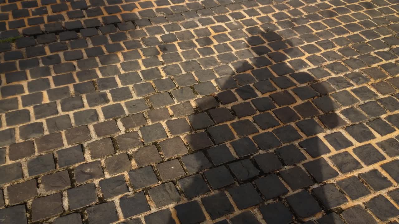 다른 사람들이 지나갈 때 자신의 그림자를 드리우면서 벽돌로 된 포장 도로에 서서 자신의 그림자를 드리우는 남자