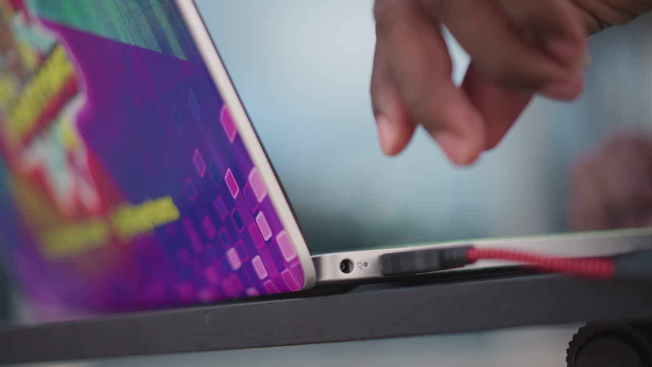 colorful laptop corner with red cable, dj connecting audio on stickered deck for rooftop set, vivid backlit keys and skyline blur, hands working quickly, upbeat festival vibe and creative energy