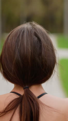 back view of sporty woman in black top jogging through park with blurred green background, ideal for fitness, exercise, and outdoor running content showcasing athletic movement and health lifestyle