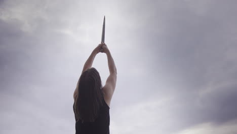 Liberated-woman-with-bare-arms-holds-sword-up-to-sky,-energy-healer