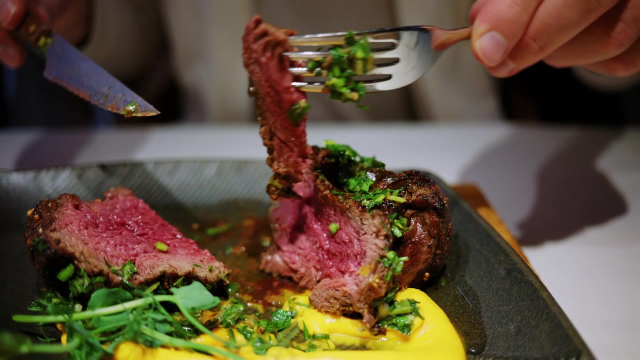 Nahaufnahme eines medium gebratenen Steaks, das in einem Restaurant aufgeschnitten wird.