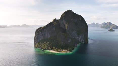 aerial view of the dramatic limestone island of pinagbuyutan, surrounded by calm turquoise sea and edged by lush tropical forest and white sandy beach in northern palawan