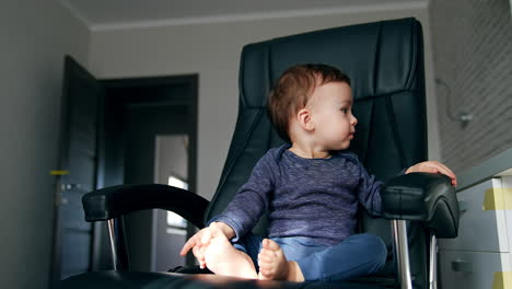 pretty happy toddler sitting in a black office chair. beautiful child turns to the table trying to reach something. low angle view.