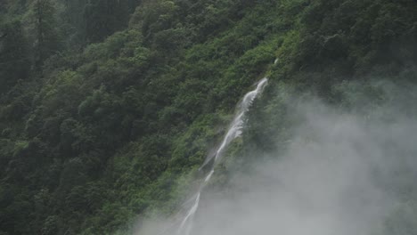 forest waterfall in nepal in the clouds, dark green atmospheric moody mountain scenery with waterfalls and green forest of trees in dark mood nature shot in himalayas mountains in nepal