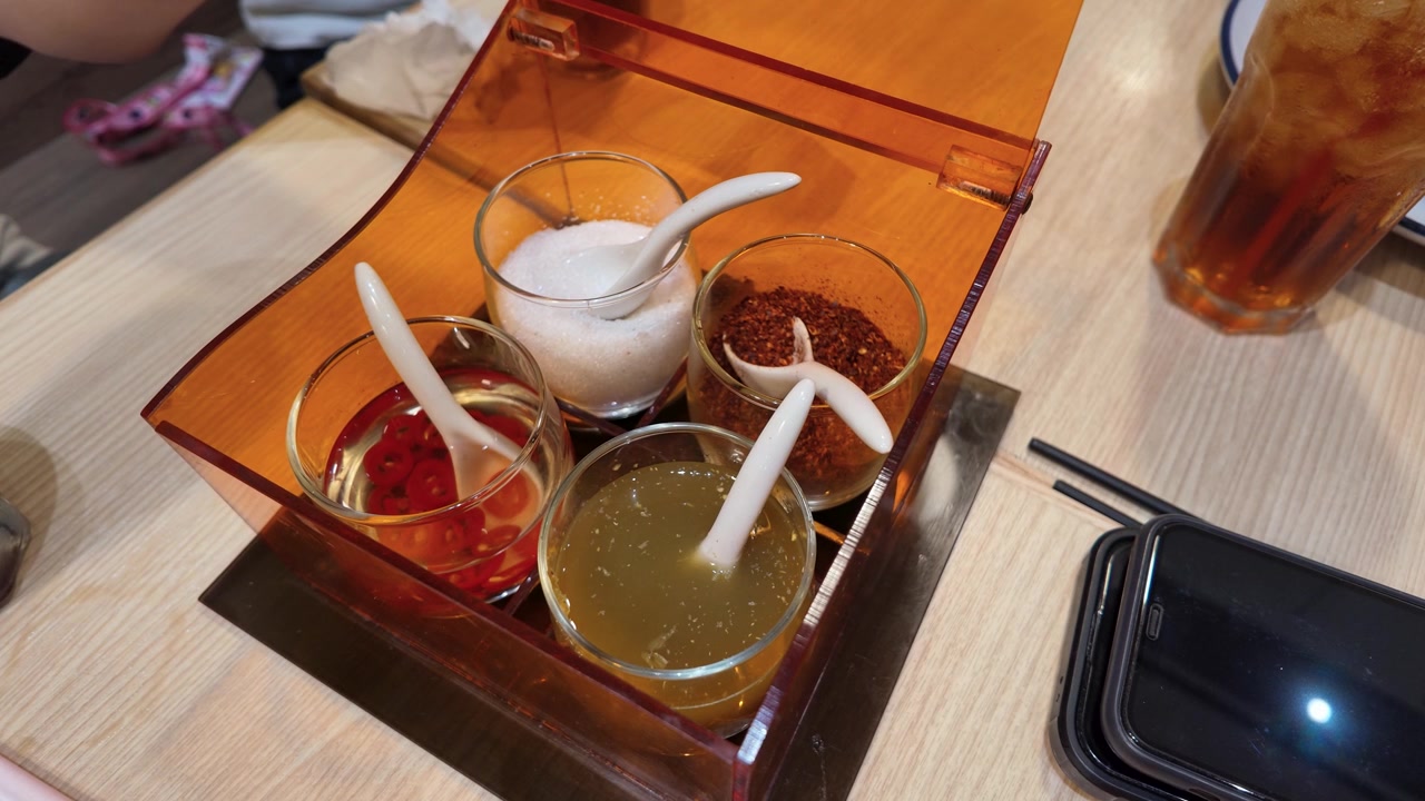 Una mano prende lo zucchero da un vassoio di condimenti tradizionale thailandese in una spaghetteria di Bangkok