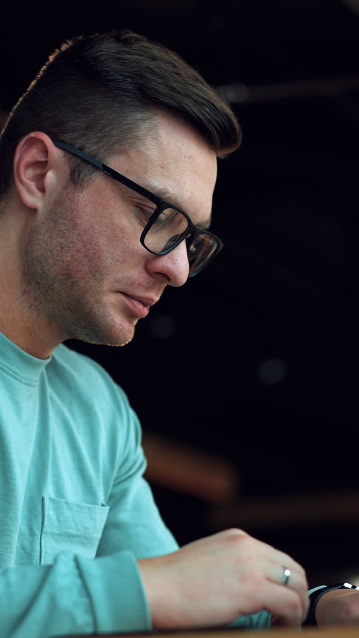 Dark-haired handsome man in glasses working on laptop. Businessman think of a job issue holding by his chin. Close up. Vertical video