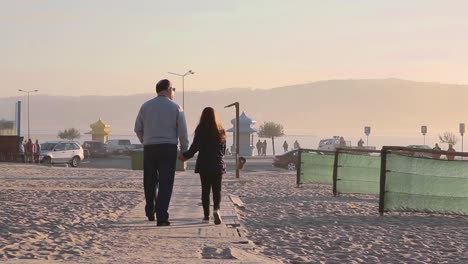 Vista-Trasera-De-La-Nieta-Y-El-Abuelo-Caminando-Tomados-De-La-Mano-Cerca-De-La-Playa-Al-Atardecer