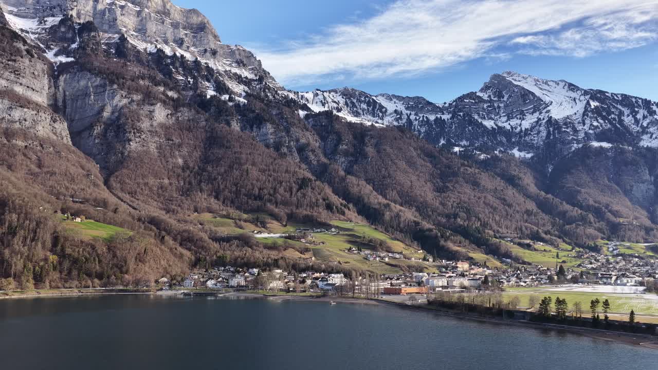 Walensee, Svizzera. Ripresa drone in avvicinamento sul lago verso un villaggio alpino, montagne, cielo blu, natura europea suggestiva.