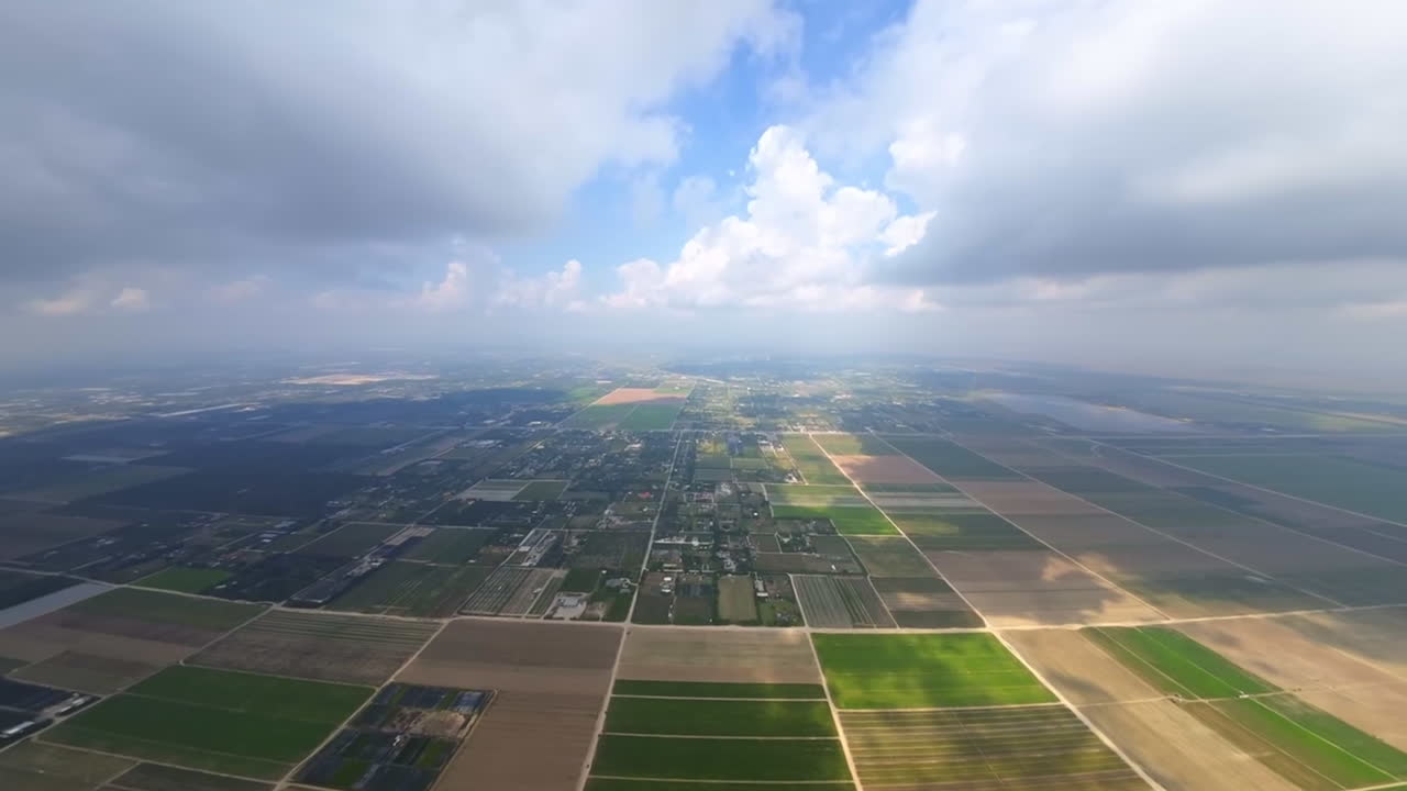 Vast farmlands and rural inhabited areas from top view. FPV drone footage of the land through clouds.