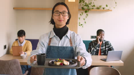retrato de un camarero sosteniendo una bandeja de comida y sonriendo a la cámara en una cafetería