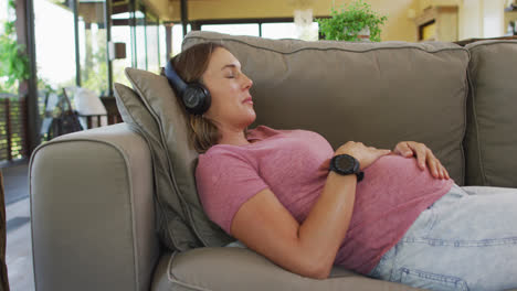 relaxed caucasian pregnant woman lying on sofa and listening to music