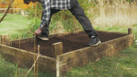 young man using trowel making row for sowing seeds raised garden bed