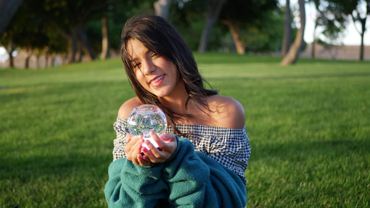 una linda joven hispana sonriendo alegremente en un parque con una bola de cristal mágica