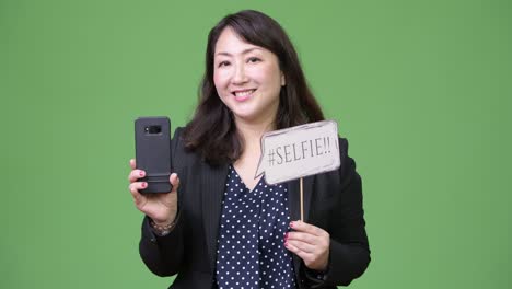 mature beautiful asian businesswoman showing phone and paper sign