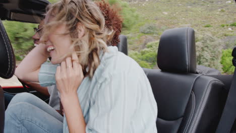 group of young friends in back of open top hire car on summer vacation