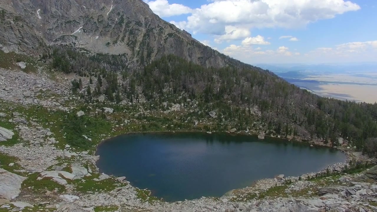 Forward tracking shot down a mountainside towards a pond