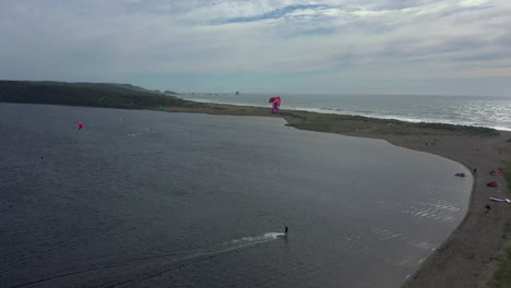 Kitesurfistas-Tirados-A-Través-De-Las-Tranquilas-Aguas-Del-Lago-Floras-Por-Power-Kite-Con-El-Océano-Pacífico-Dividido-Por-Una-Franja-De-Playa