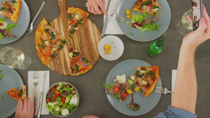 Vista aérea de amigos en un restaurante de pizza comiendo y haciéndose selfis con el móvil