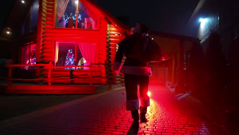 santa claus walking to thr home with gifts. santa claus in red background going to home for kids.