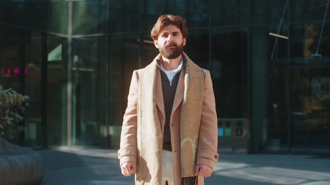 Cheerful young man tourist smiling at camera waving hands gesturing hello standing on city street