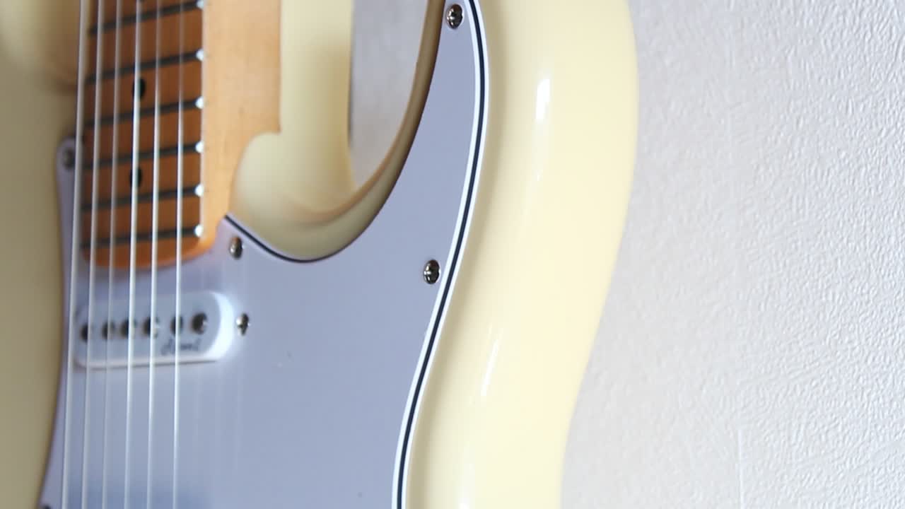 imágenes en primer plano de una stratocaster blanca crema colgando de una pared interior blanca