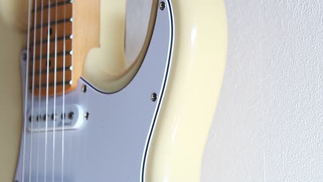 close-up footage of a cream white stratocaster hanging off a white interior wall