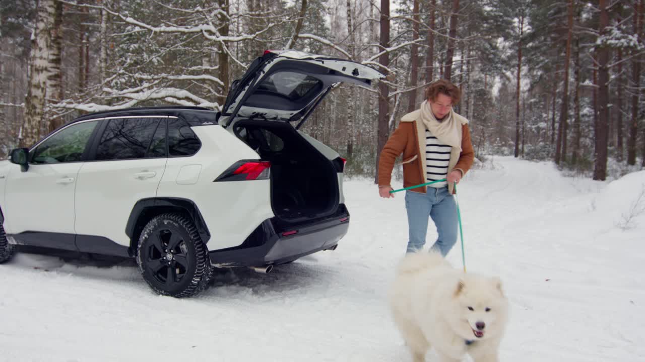 눈 덮인 숲을 산책하기 위해 사모예드 개를 트렁크에서 꺼내는 남자