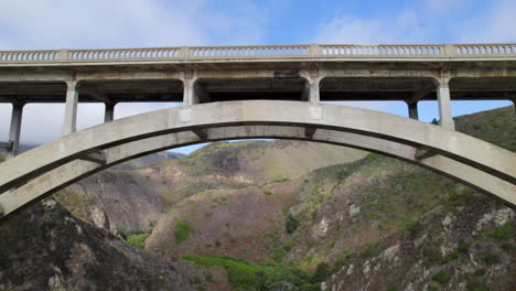 aerial flying under highway 1 to reveal bixby bridge spanning creek at big sur