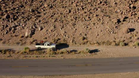 pickup driving un gravel road in desert landscape with person standing on the back bed