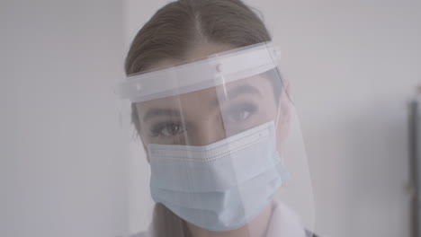 redhead doctor woman in white coat wearing medical mask and facial screen protection looking at the camera 1