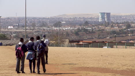 teenage school students walking home through open park with a backdrop of soweto township and the landmark cooling towers.