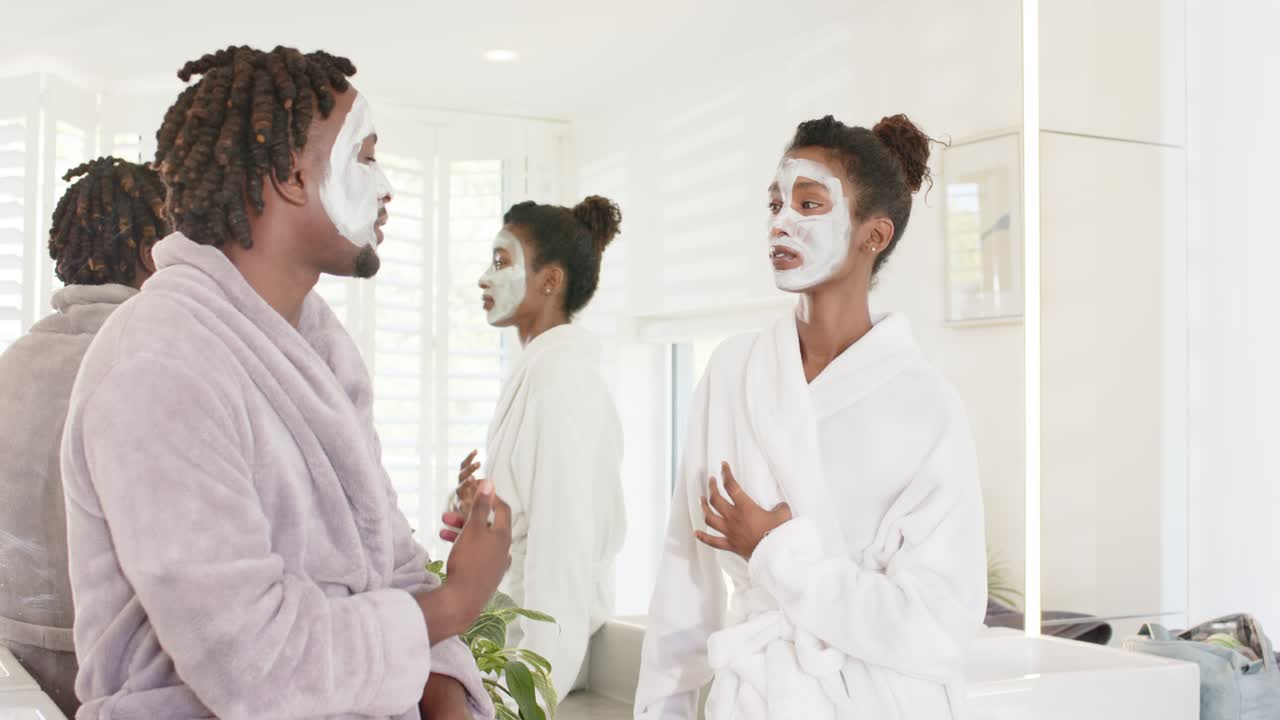 African American couple vanity, woman touching chest talking, man laughing after masks robes